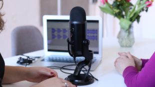 Black microphone on a white table with computer behind it